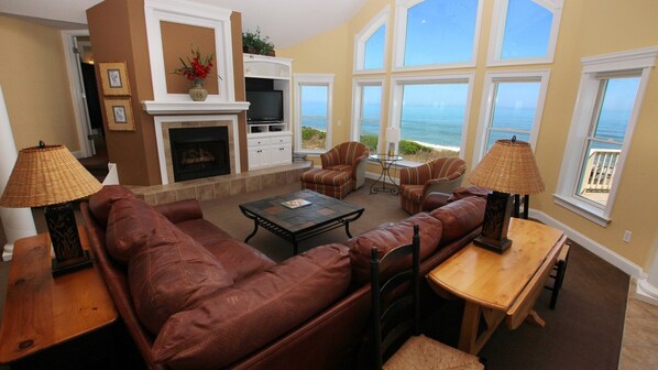 A living room with a fireplace, a television, and a view of the ocean through large windows.