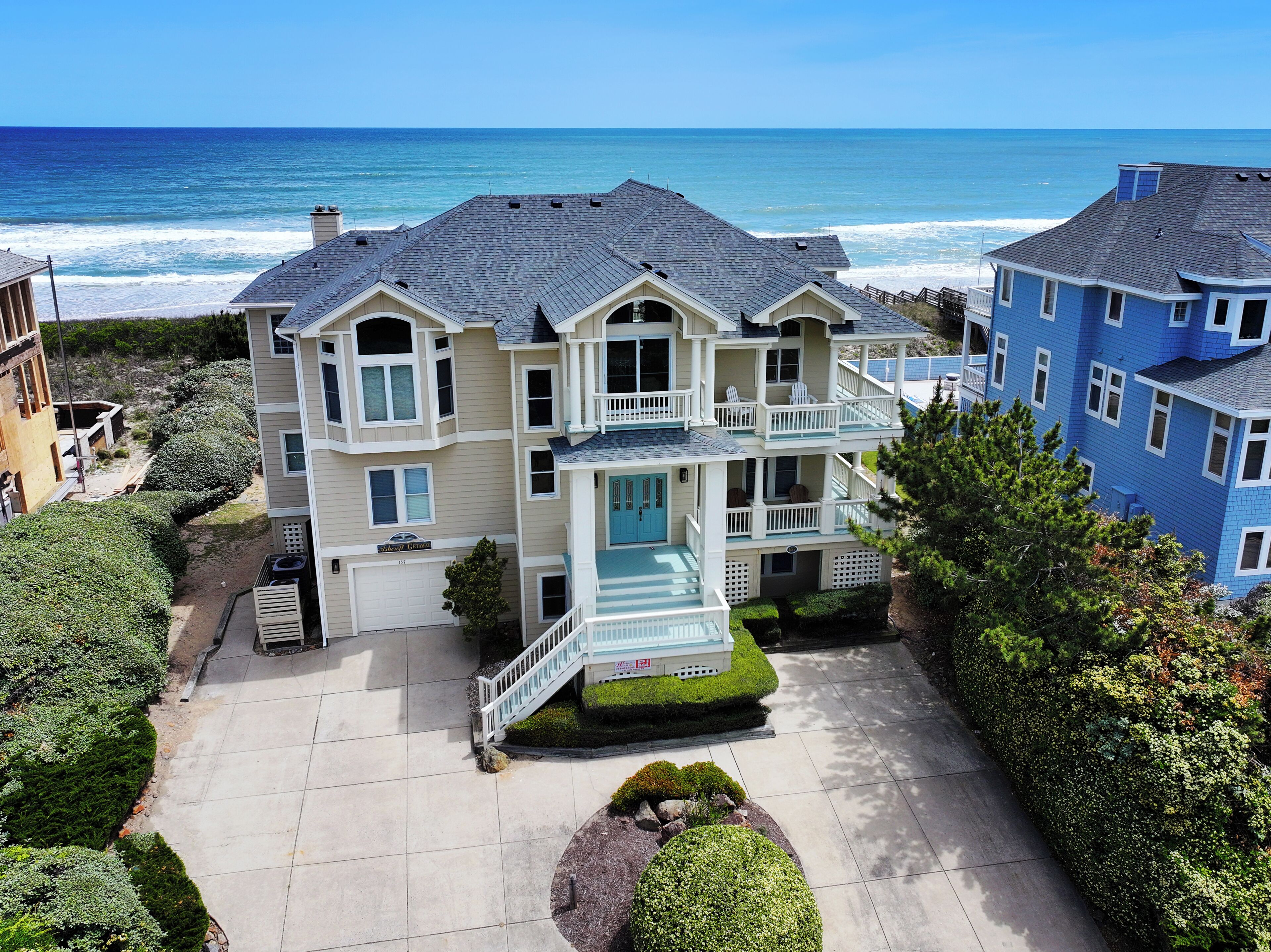 A multi-story beachfront property with a spacious driveway, a front porch, and a balcony overlooking the ocean.