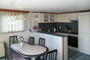 A kitchen with a dining table, chairs, a coffee maker, and a stove.