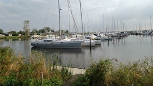 A marina with multiple sailboats docked in calm waters, surrounded by greenery and a cloudy sky.
