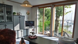 A living room with a television, a dining table, and a view of a marina through large windows.