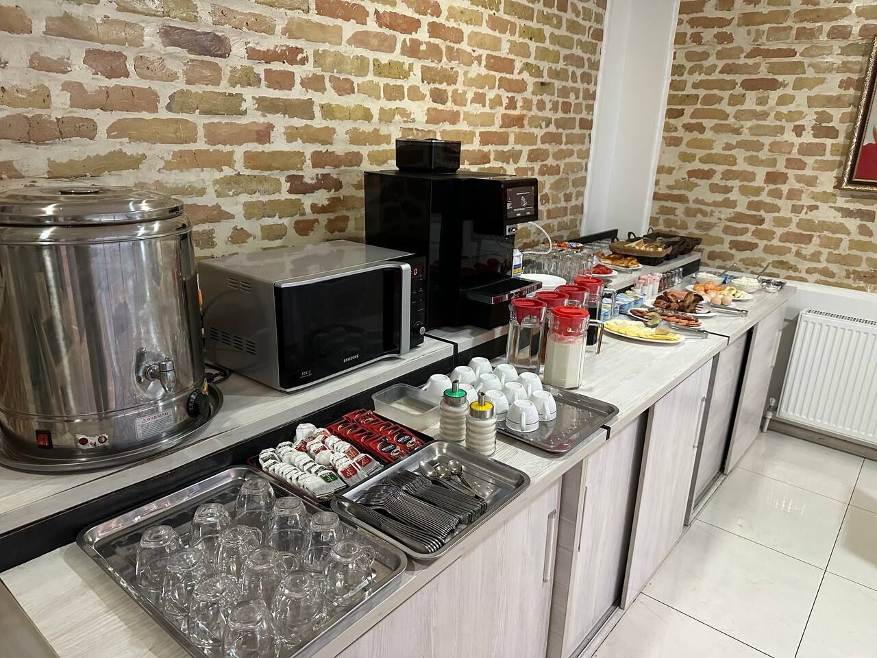 A buffet setup with a stainless steel cooler, microwave, and various food items on a counter.