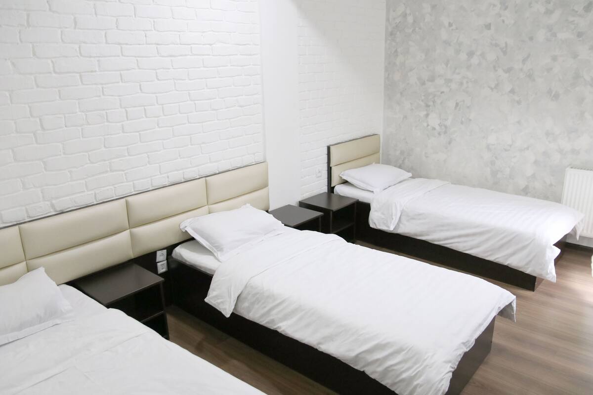 A hotel room with two single beds, a white brick wall, and a textured grey wall.