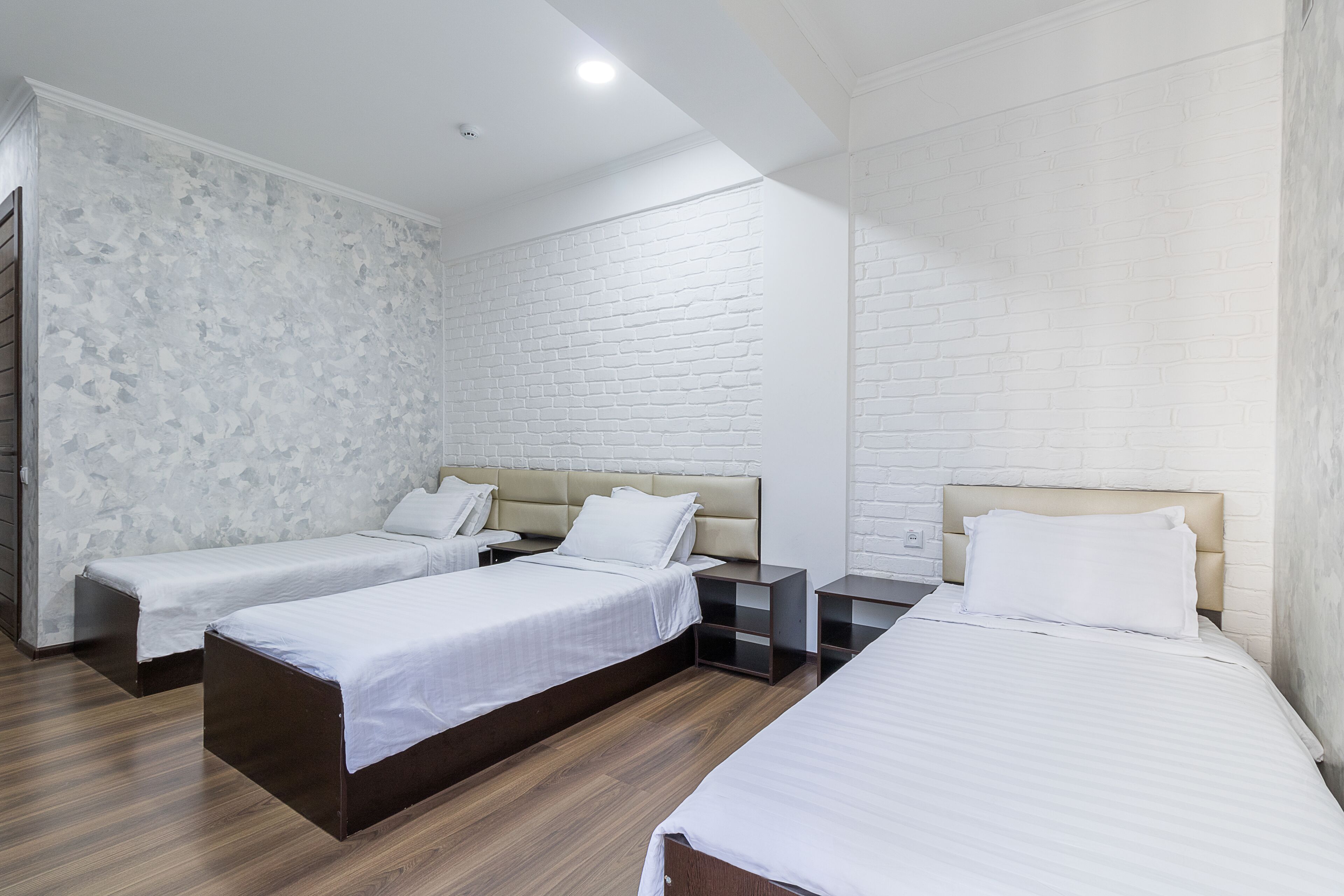 A hotel room with three beds, white brick walls, and wooden flooring.