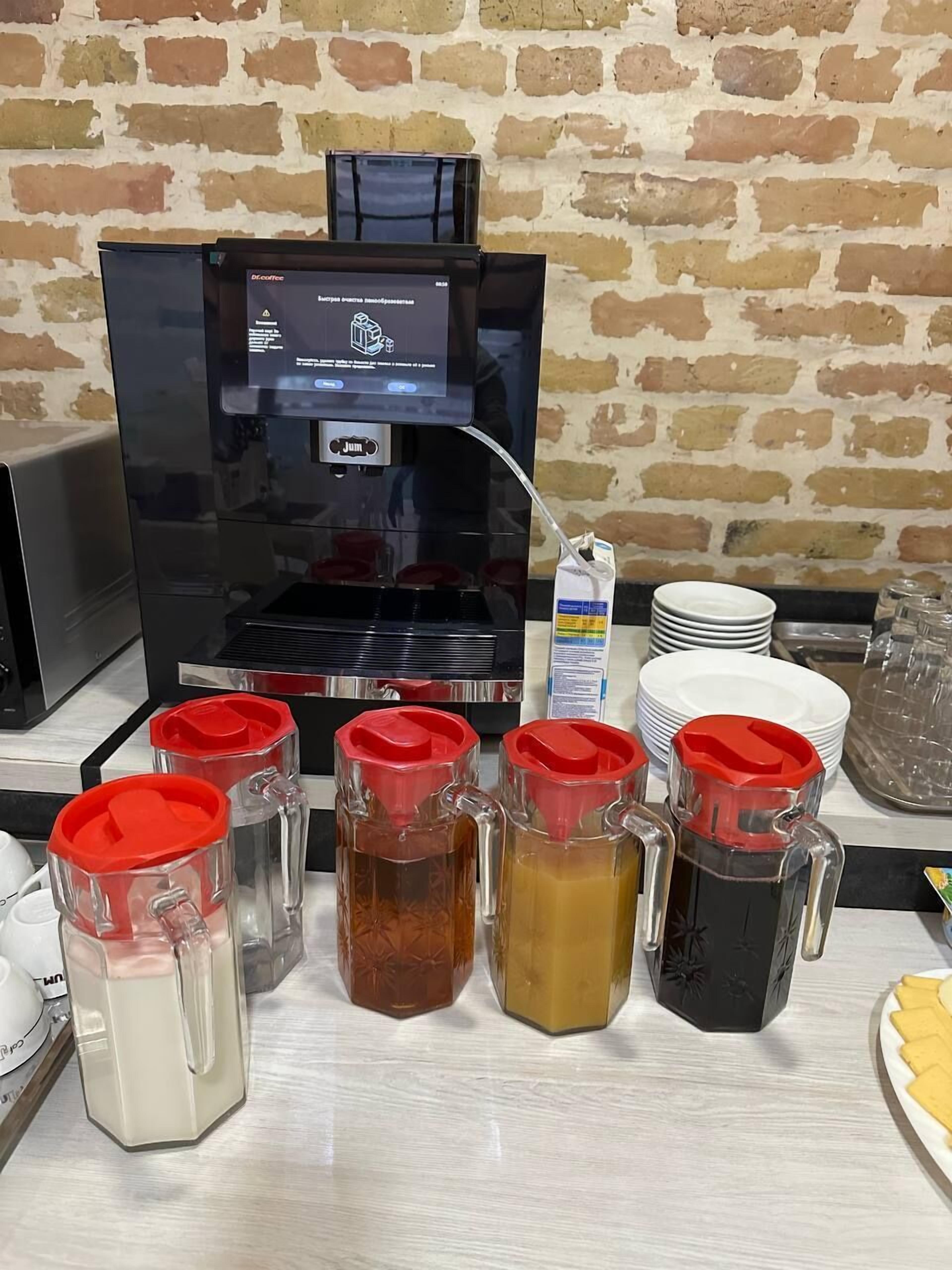 A coffee station with a coffee machine, various drink dispensers, and stacked white plates.