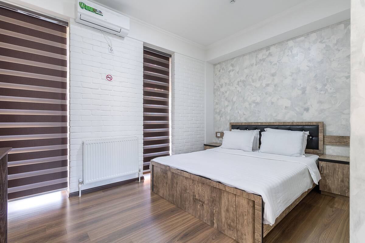 A bedroom with a wooden bed, white bedding, a radiator, and a brick-patterned wall.