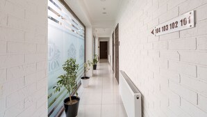 A hallway with white brick walls, potted plants, and a directional sign. - Orion Hotel (Tashkent)