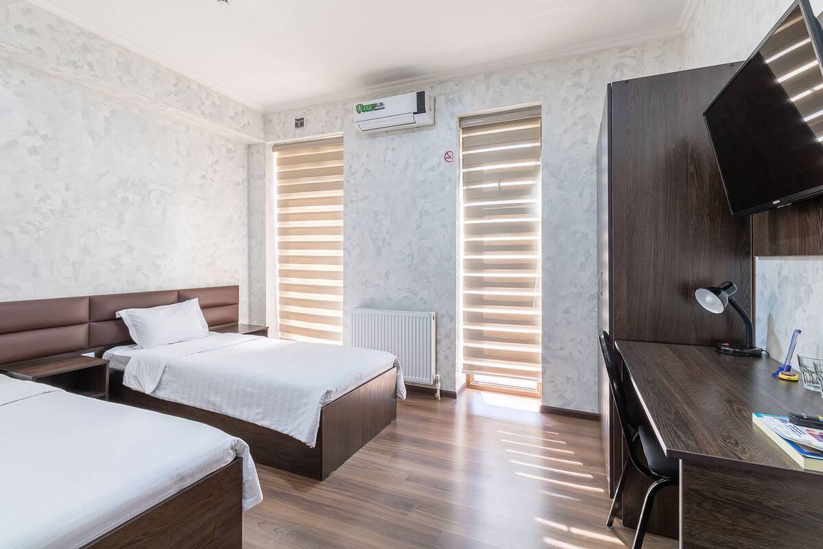 A hotel room with two beds, a desk, a chair, a TV, and a radiator.