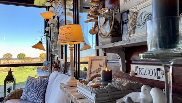 A cozy room with a wicker sofa, a 'WELCOME' sign, decorative items, and a view of the outdoors.