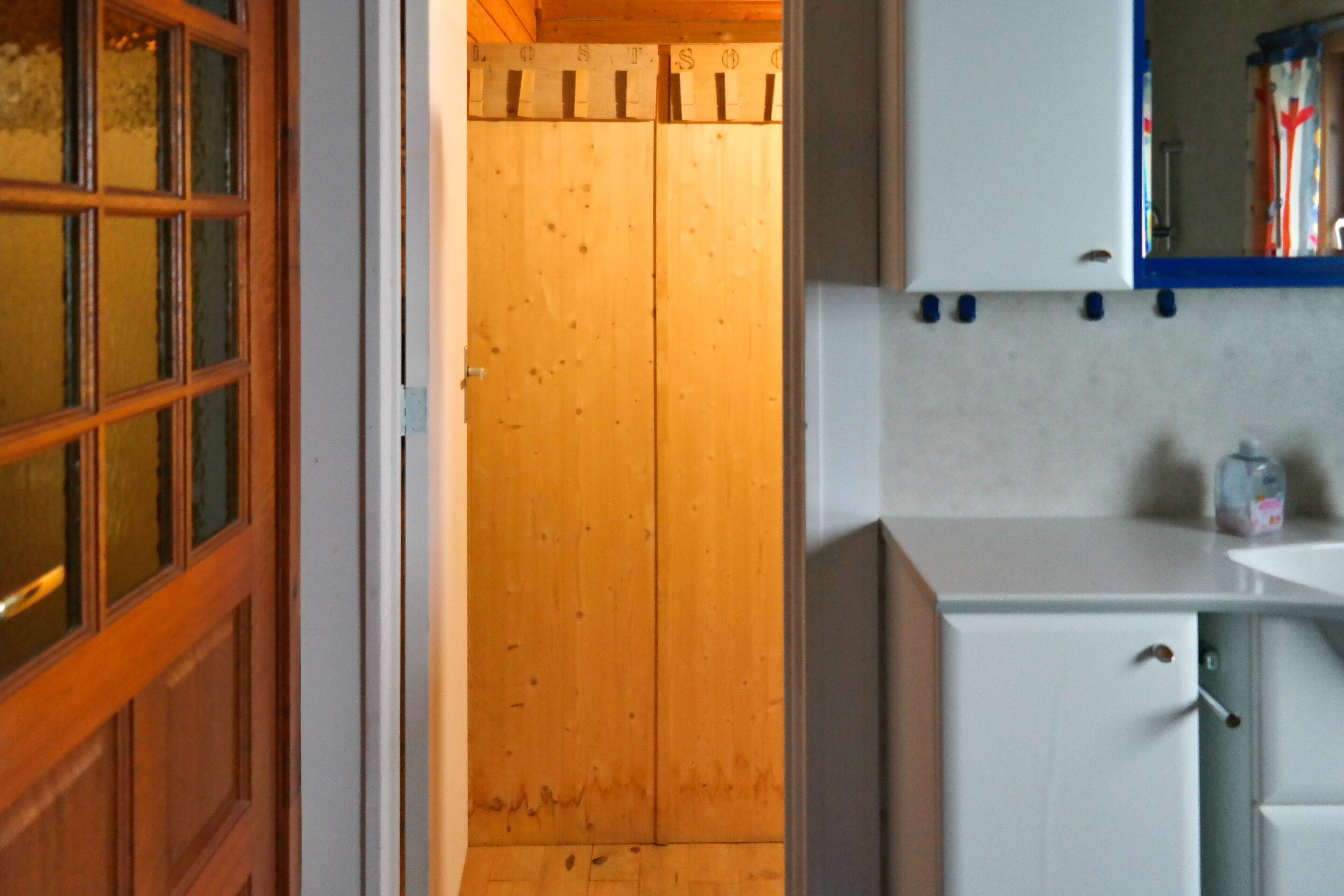 Eine Holztür mit Milchglasscheibe, ein weißes Schränkchen mit Spiegel und ein Regal mit einer Flasche.