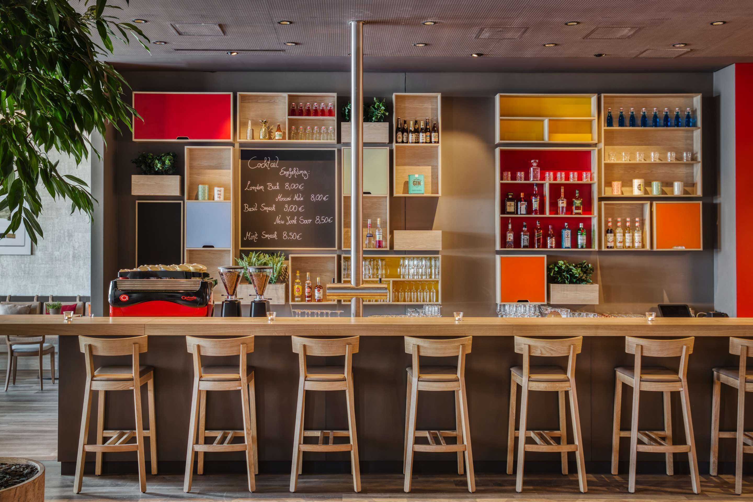 A bar area with wooden stools, shelves of bottles, and a chalkboard menu.