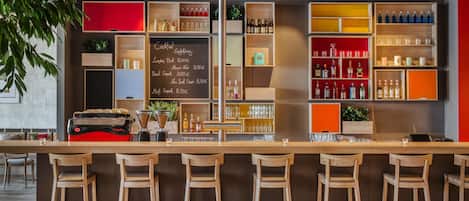 A bar area with wooden stools, shelves of bottles, and a chalkboard menu.