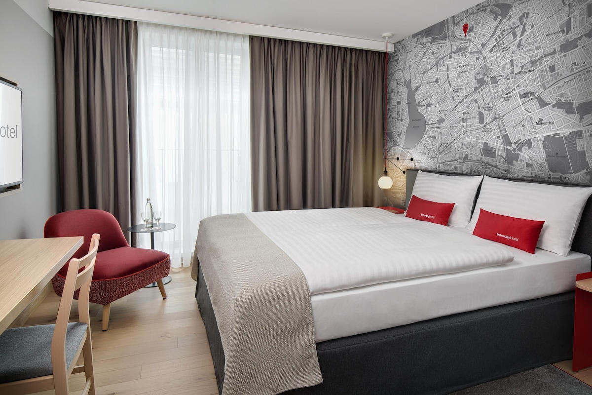 Een hotelkamer met een bed, een bureau, een stoel en een kaart aan de muur.