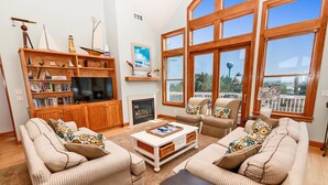 A living room with striped sofas, a coffee table, a TV, bookshelves, and large windows with a view. - Soundside, Private Pool, Rec Room, Hot Tub, CC204, Aqua Holic (Corolla)