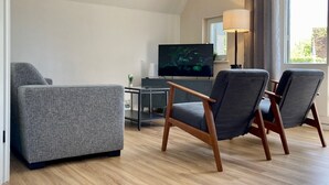 Una sala de estar moderna con un sofá gris, dos sillones, un televisor de pantalla plana, una mesita y una lámpara.