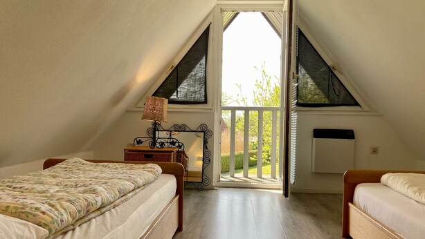 Un dormitorio con dos camas, una ventana que da a zonas verdes, un radiador y una pequeña mesa con lámpara.