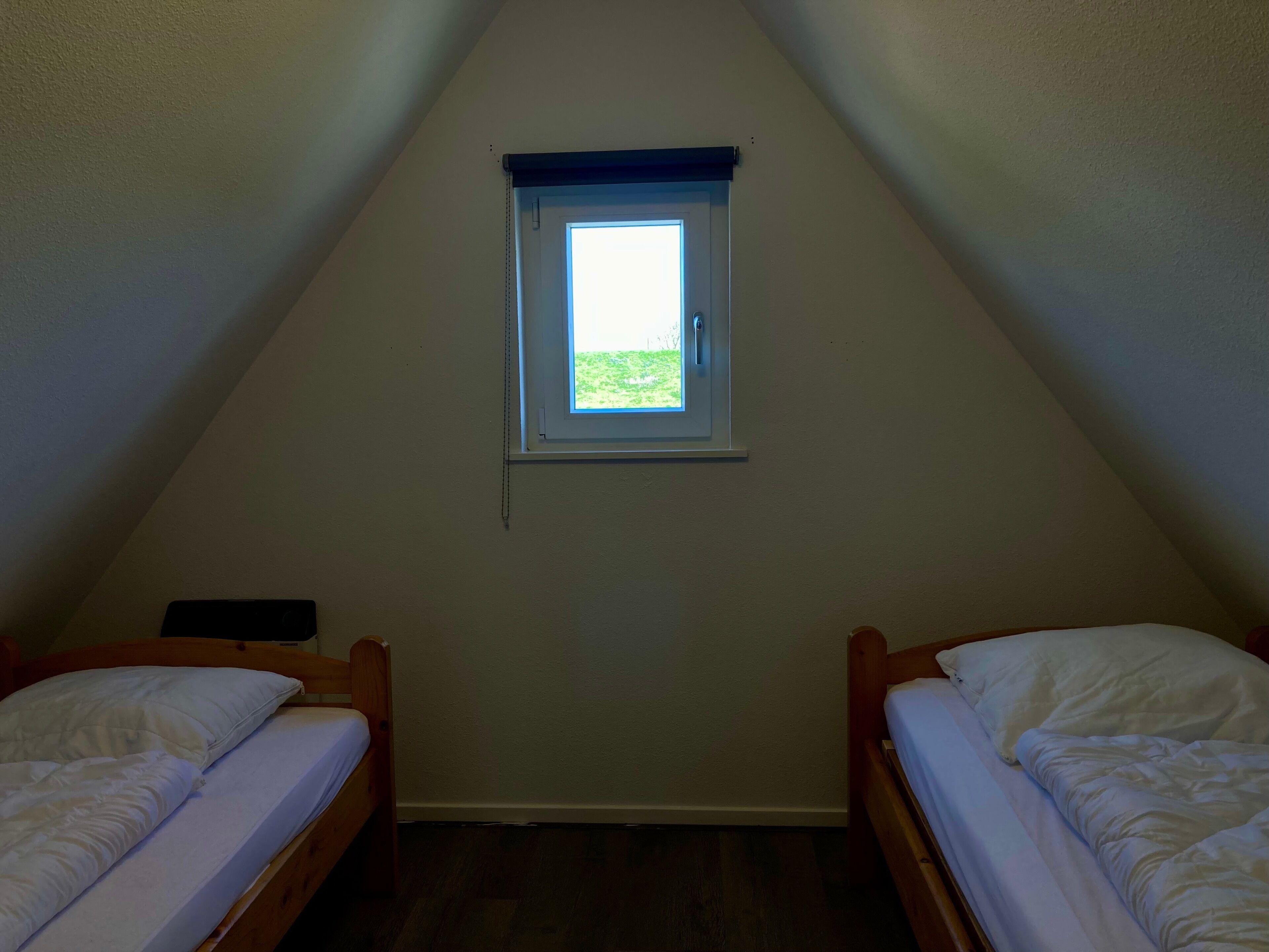 Een kleine, driehoekige kamer met twee eenpersoonsbedden, een raam met uitzicht op groen en een schuine kap.