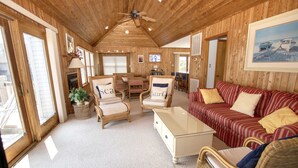 Ein gemütliches Blockhaus-Interieur mit Holzwänden, einem Essbereich, einem Wohnzimmer mit Sofa und Sesseln sowie einem Deckenventilator.