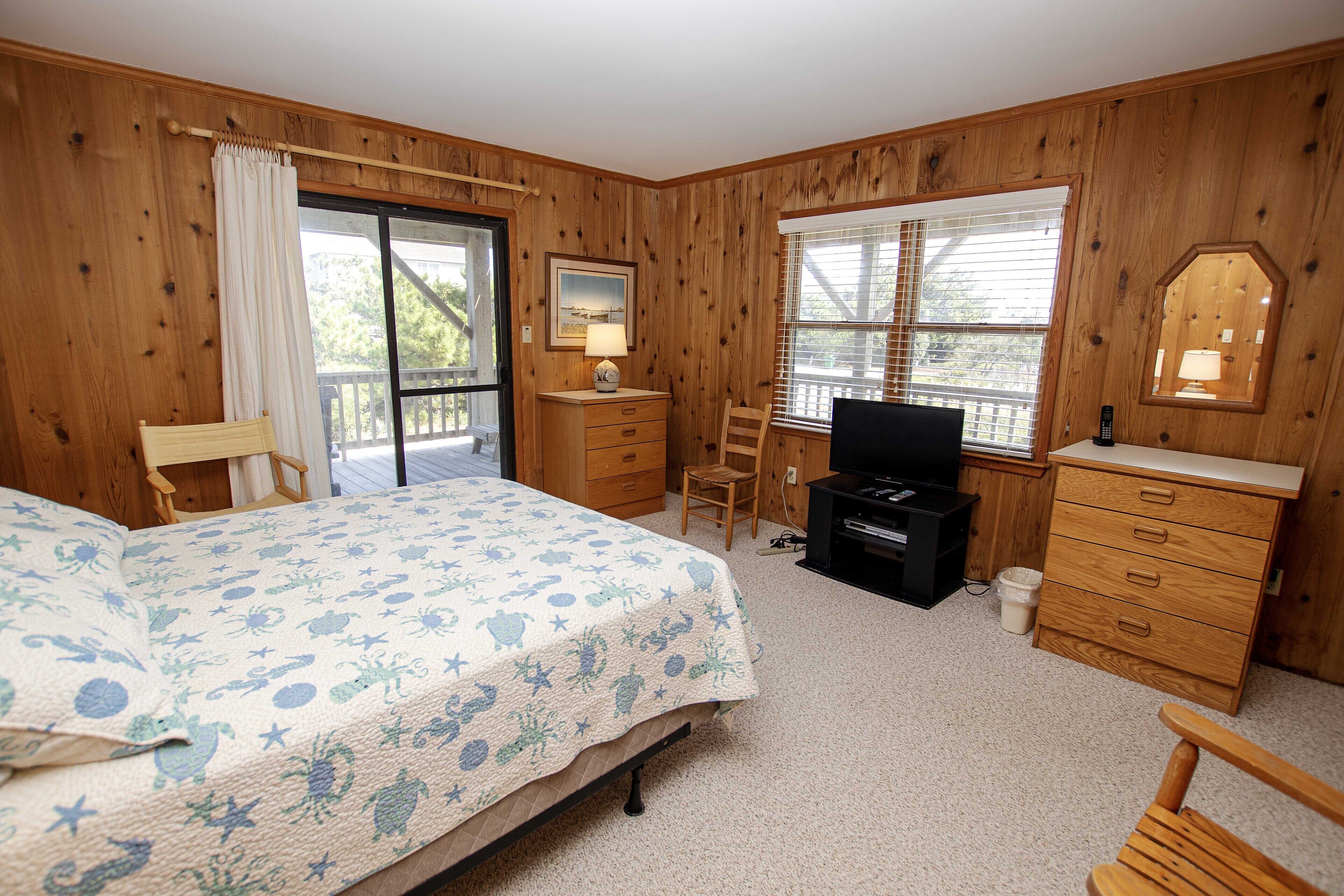 A bedroom with a bed, a desk, a chair, a dresser, and a television.