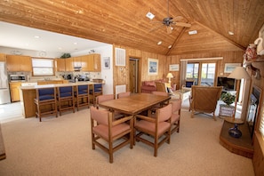 A spacious living area with a wooden ceiling, a dining table with chairs, a sofa, and a television.