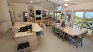 A spacious living area with a kitchen, dining table, and a balcony with ocean views. - OCEANFRONT, Pool, Priv Beach Access, Rec Rm, WL945, Sweet Dreams (Corolla)