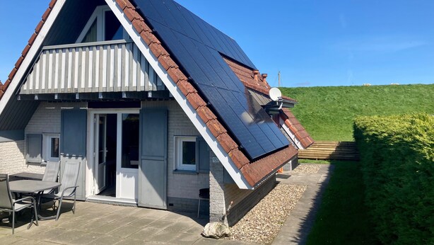 A house with a sloped roof, solar panels, a satellite dish, and a patio with outdoor furniture. - Cozy Holiday Home by the Dike in a Quiet Location at Lauwersmeer (Anjum)
