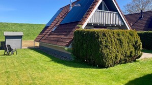 A triangular-roofed building with a balcony, surrounded by well-maintained grass and a hedge. - Cozy Holiday Home by the Dike in a Quiet Location at Lauwersmeer (Anjum)