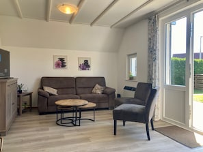 A living room with a sofa, armchair, round table, and a television on a cabinet.