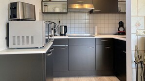 A compact kitchen with a built-in microwave, kettle, and coffee maker, featuring dark cabinetry and a tiled backsplash. - Cozy Holiday Home by the Dike in a Quiet Location at Lauwersmeer (Anjum)
