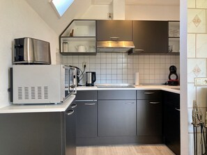 A compact kitchen with a built-in microwave, kettle, and coffee maker, featuring dark cabinetry and a tiled backsplash. - Cozy Holiday Home by the Dike in a Quiet Location at Lauwersmeer (Anjum)