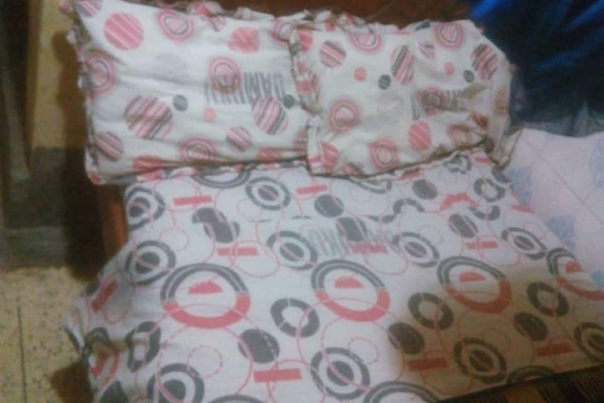 A bed with a patterned bedspread and pillows, a wooden headboard, and a blue blanket on the right side.