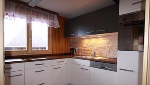 Cozinha compacta com armários brancos, painel de backsplash de pedra e forno de aço inoxidável.