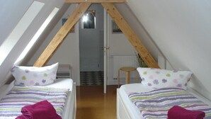 Ein kleines, dreieckiges Schlafzimmer im Dachgeschoss mit zwei Betten, jedes mit einem floralen Kissen und einem zusammengerollten Handtuch.