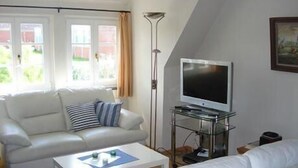 Ein Wohnzimmer mit einem weißen Sofa, einem Couchtisch und einem Flachbildfernseher auf einem Glaskonstruktion-Ständer.