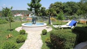 A landscaped garden with a fountain, a stone pathway, and lounge chairs. - Ferienwohnung Ginkgo A3 (Medulin)