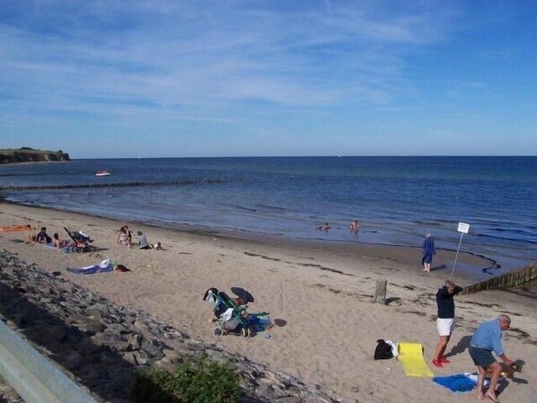 A beach with people sunbathing, swimming, and walking along the shore.