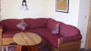 A cozy living room with a red sofa, a wooden coffee table, patterned cushions, a hanging light fixture, and a framed painting on the wall. - Zur Alten Schmiede II Wohnung Oben II (Boltenhagen)