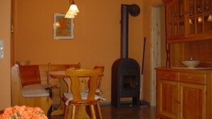 A cozy room with a wooden dining table, chairs, a sofa, a fireplace, and a cabinet with glass doors. - Haus Koralle Wohnung Rechts (Boltenhagen)