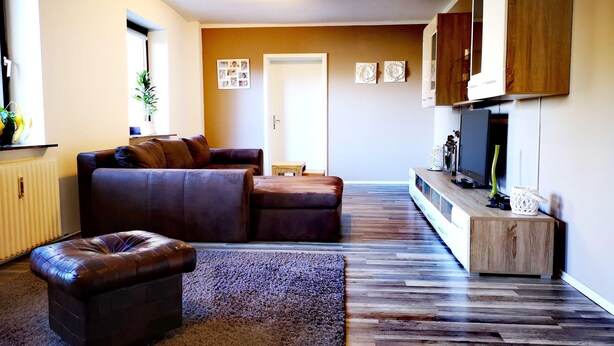 A living room with a brown leather sofa, a wooden coffee table, and a TV on a wooden stand.
