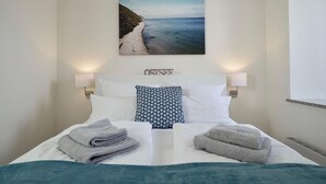 Un lit bien fait, avec vue sur la plage, et le mot « OSTSEE » inscrit sur la tête de lit.