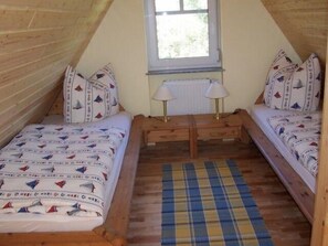A small, cozy attic bedroom with two single beds, a window, and a wooden bench.