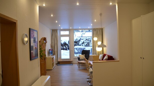 Een hotelkamer met een houten vloer, een bureau met stoel, een bed, een kast en een groot raam met uitzicht op sneeuw.