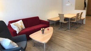 Een moderne woonkamer met een rode bank, een grijze fauteuil, een houten salontafel en een eethoek met een tafel en stoelen.
