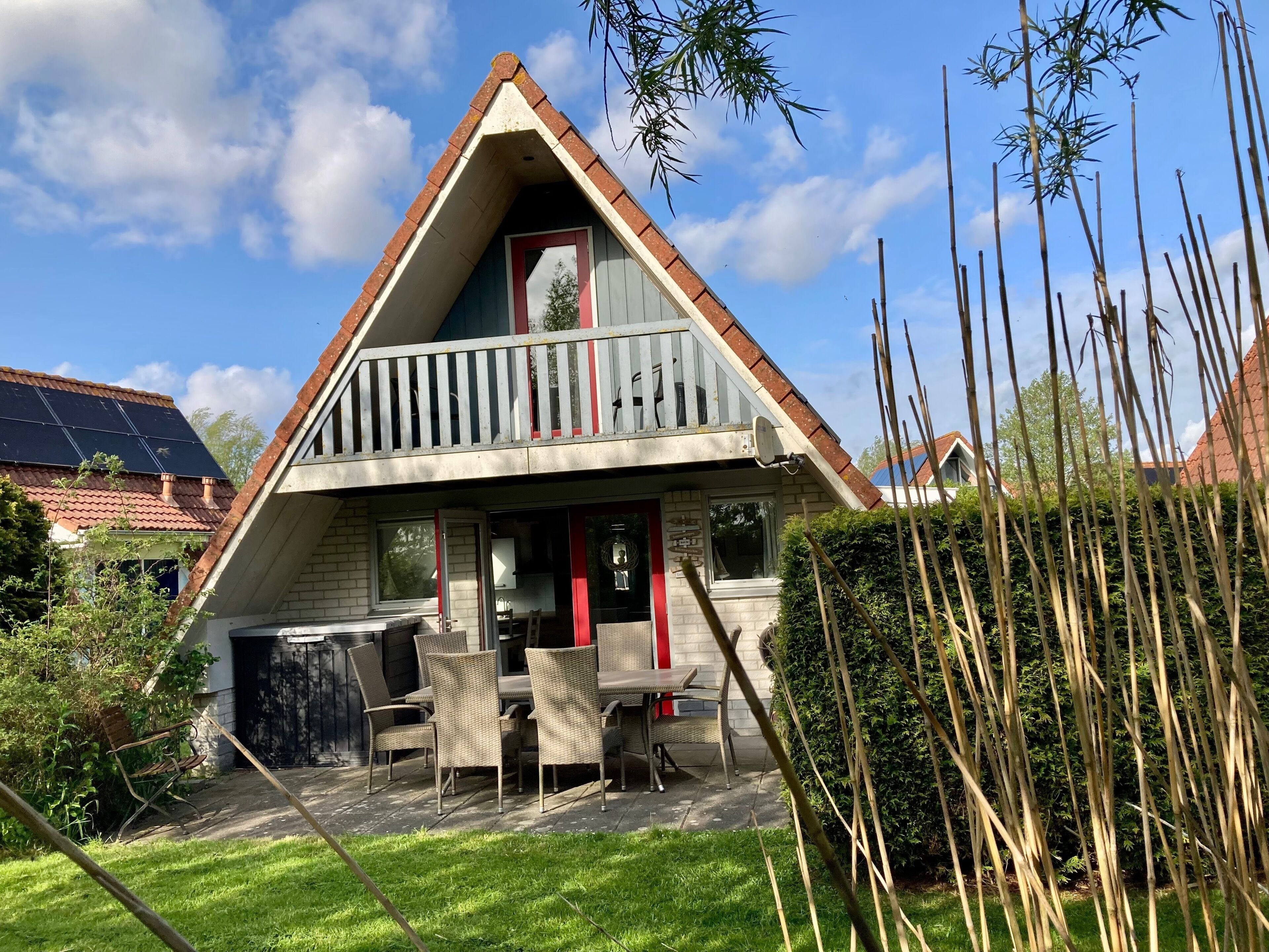 Ein zweistöckiges Haus mit Balkon, Solaranlage und Essbereich mit Gartenmöbeln.
