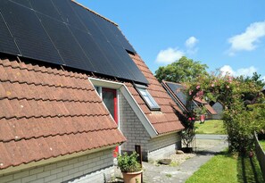 A residential building with solar panels on the roof, a red door, and a small garden with flowers. - Holiday Home Urlaubsruhe 6 p Near Lake Lauwersmeer - no Pets (Anjum)