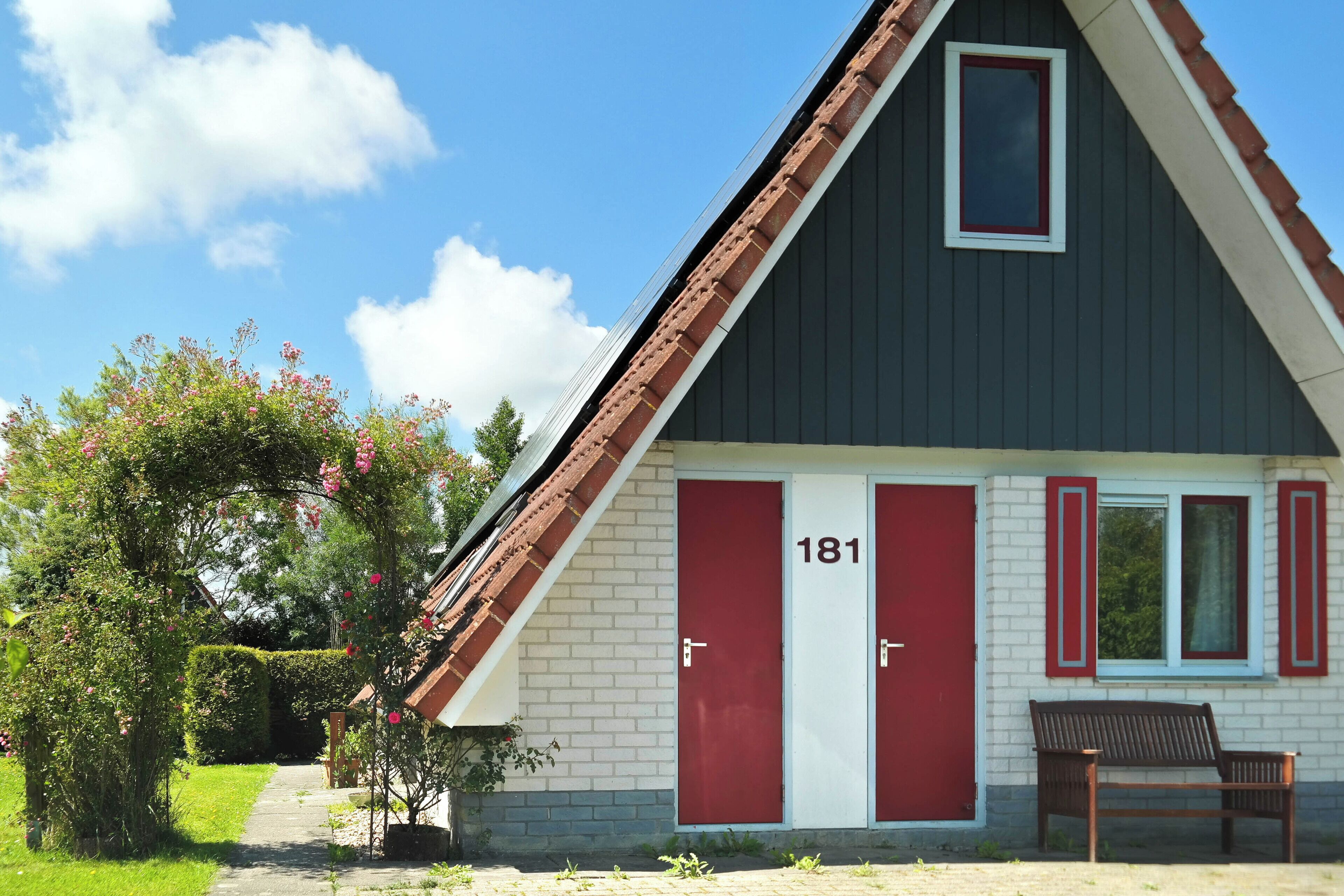 A building with a red door marked "181" and a bench outside.