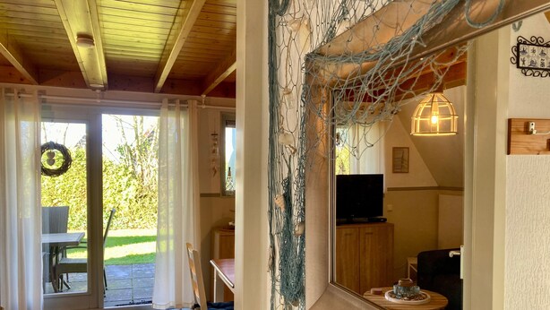 A room with a wooden ceiling, a mirror reflecting a TV and a lamp, a door leading outside, and a chair by the door.