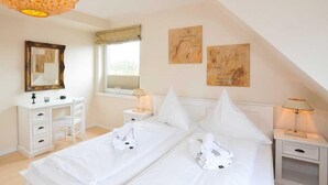 A hotel room with a large bed, a desk, a chair, a mirror, and two bedside tables with lamps. - Meerwievke (Sylt)