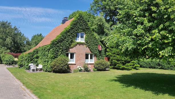 A house with a sloped roof covered in ivy, surrounded by lush greenery. - Gästehaus Zur Alten Post - Landhaus EG (Dornum)