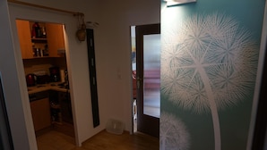 A kitchen with wooden cabinets, a coffee maker, and a refrigerator. There is a door leading to another room with a patterned wall. - Ehlershus (Reit im Winkl)